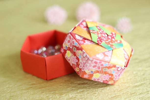 open origami colorful hexagonal box with lid with three blurred pink flowers in background