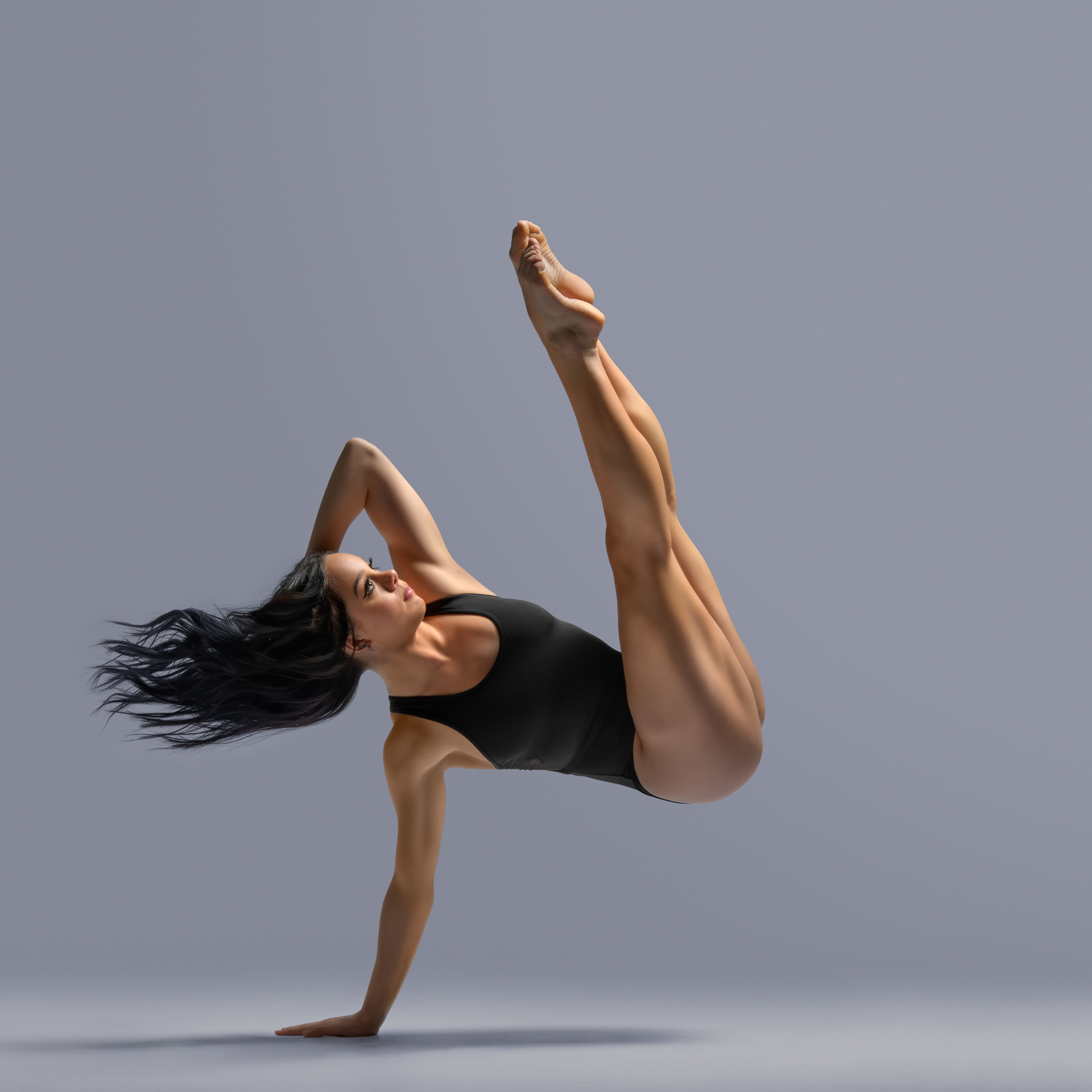 Woman dancer in black leotard posing with one hand on the ground and body lifted in the air in an abstract position